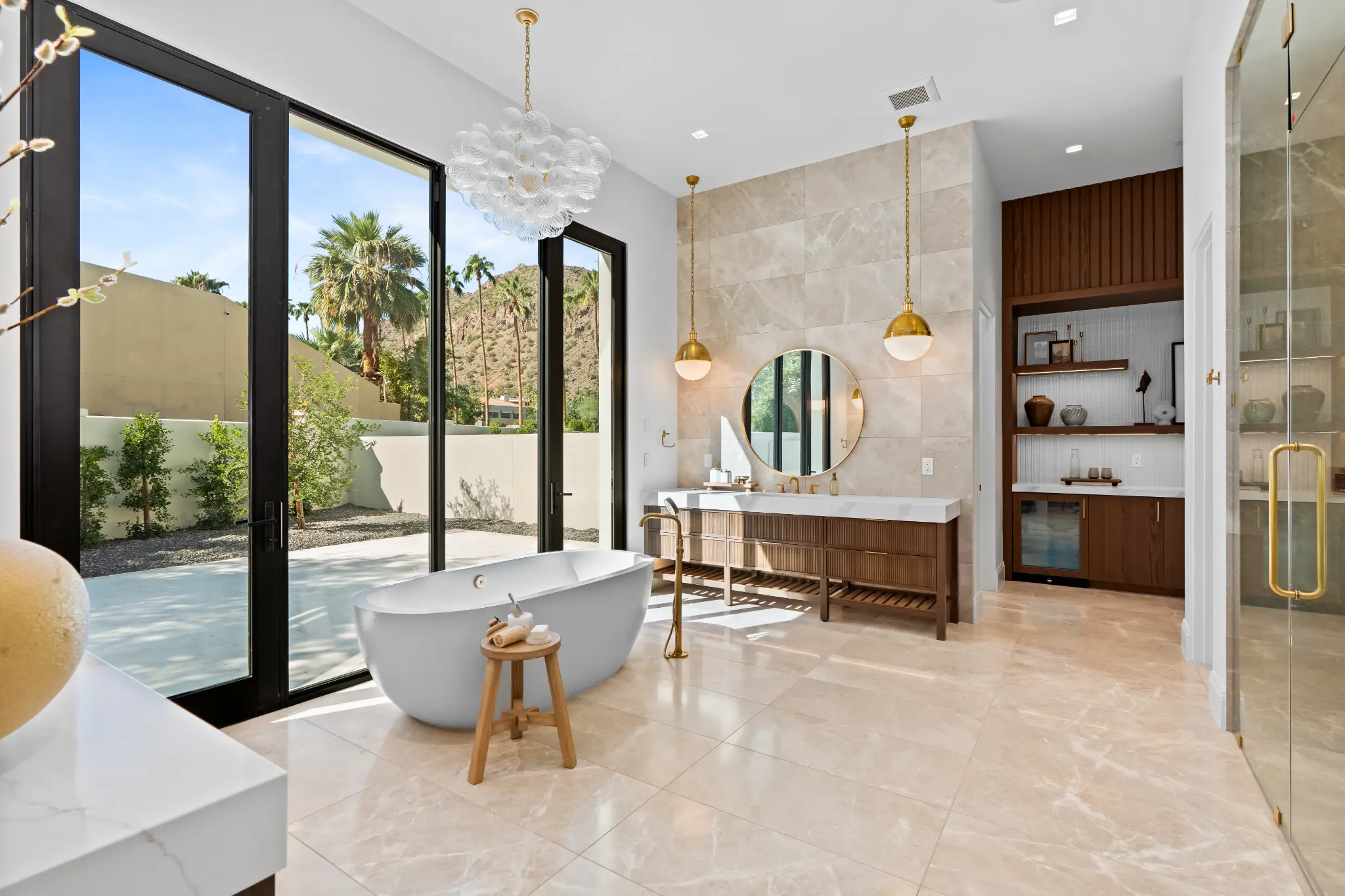 Luxury primary bathroom with freestanding tub, gold fixtures, and floor-to-ceiling windows