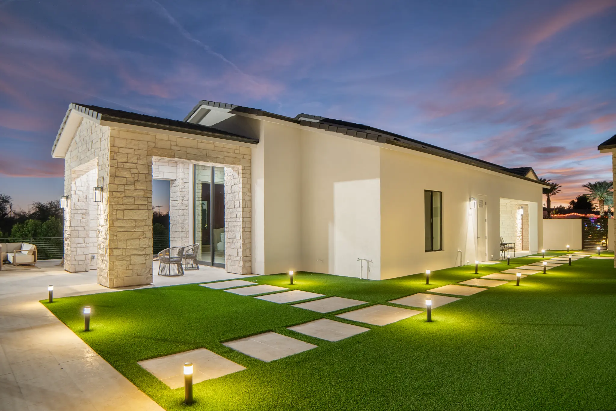 Modern desert exterior with limestone columns, illuminated stepping stone path, and turf at twilight