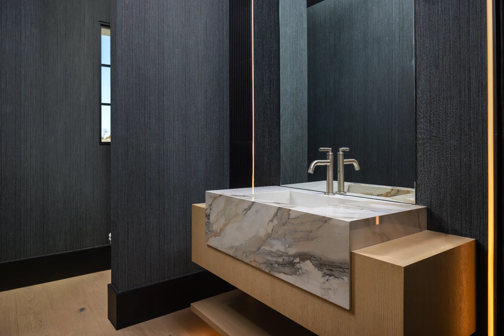 Custom stone vanity with book-matched marble, fluted wood base, and ambient lighting detail