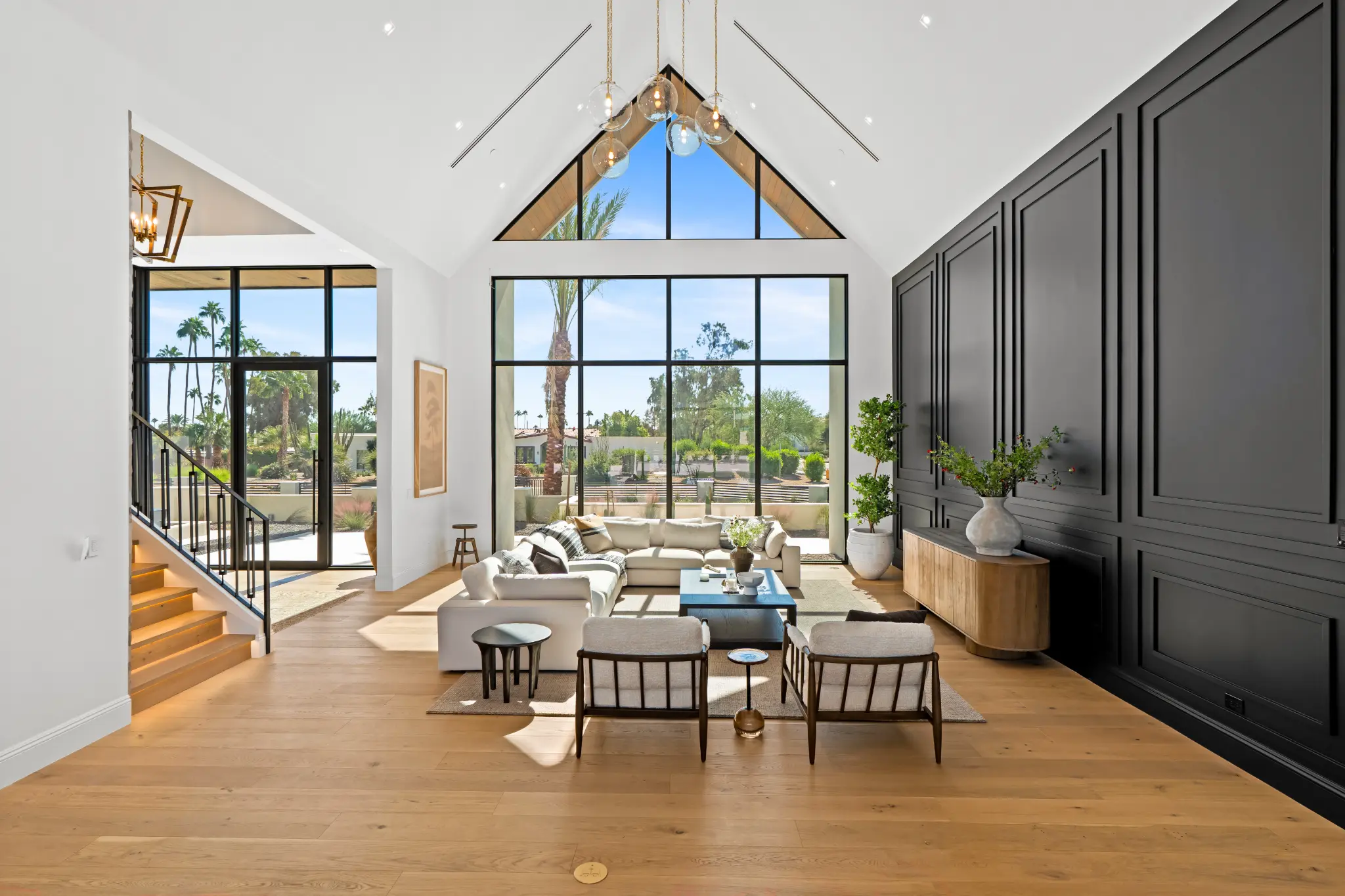 Vaulted great room with steel-framed windows, architectural wall paneling, and hardwood floors
