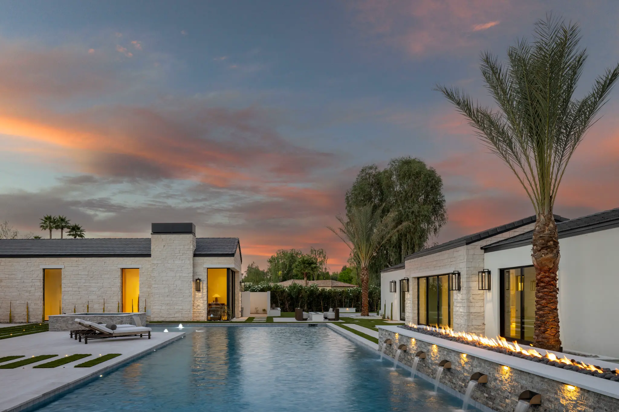 Luxury estate pool with linear fire feature, stone coping, and palm-lined grounds at sunset